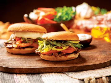 Dos sándwiches con carne, tomate y porotos verdes sobre una tabla de madera