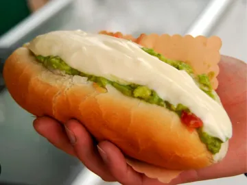 Completo con palta, tomate y mayonesa servido en la mano